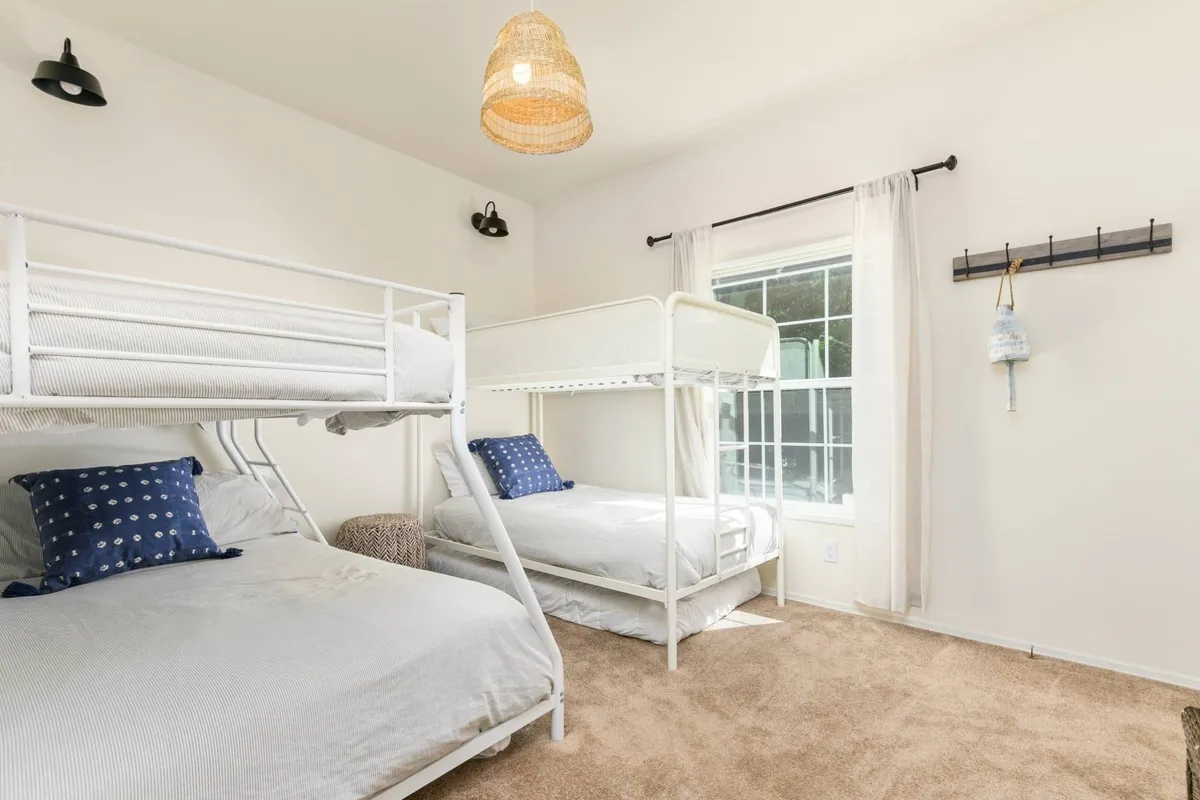 A fun and inviting bunk room with two bunk beds, decorative pillows, and a unique hanging light fixture. The playful design and cozy bedding create a welcoming space perfect for kids or groups, encouraging late-night stories or games.