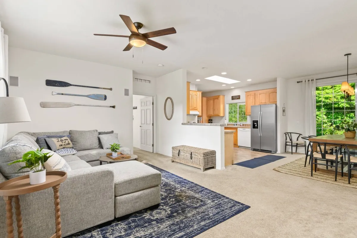 The image showcases an inviting open-concept living space with a plush sofa, a spacious dining table set for gatherings, a modern kitchen perfect for shared meals, and large windows offering tranquil views of the lake just outside.