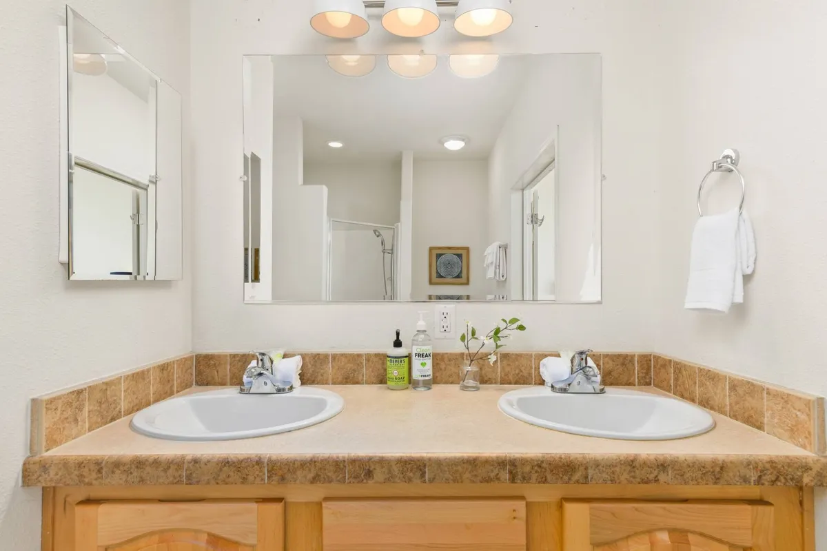 A modern bathroom featuring dual sinks, a large mirror, and vanity lighting. The space is calm, organized, and ideal for shared morning or nighttime routines, reflecting the description of the spacious shared full bath.