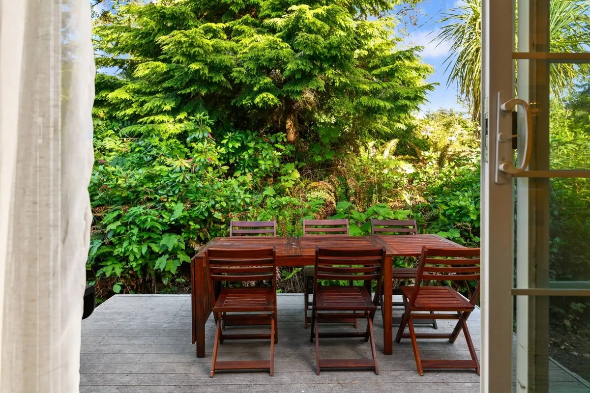 A tranquil outdoor dining area with a wooden table and comfortable chairs set amidst lush greenery. The scene radiates a welcoming atmosphere, ideal for enjoying meals outdoors while surrounded by nature.