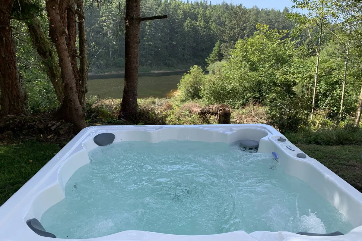 A tranquil outdoor scene featuring a hot tub overlooking the lake, surrounded by lush trees. The calm water reflects the colors of the sunset, creating an inviting atmosphere perfect for relaxation after a day of lakeside fun.
