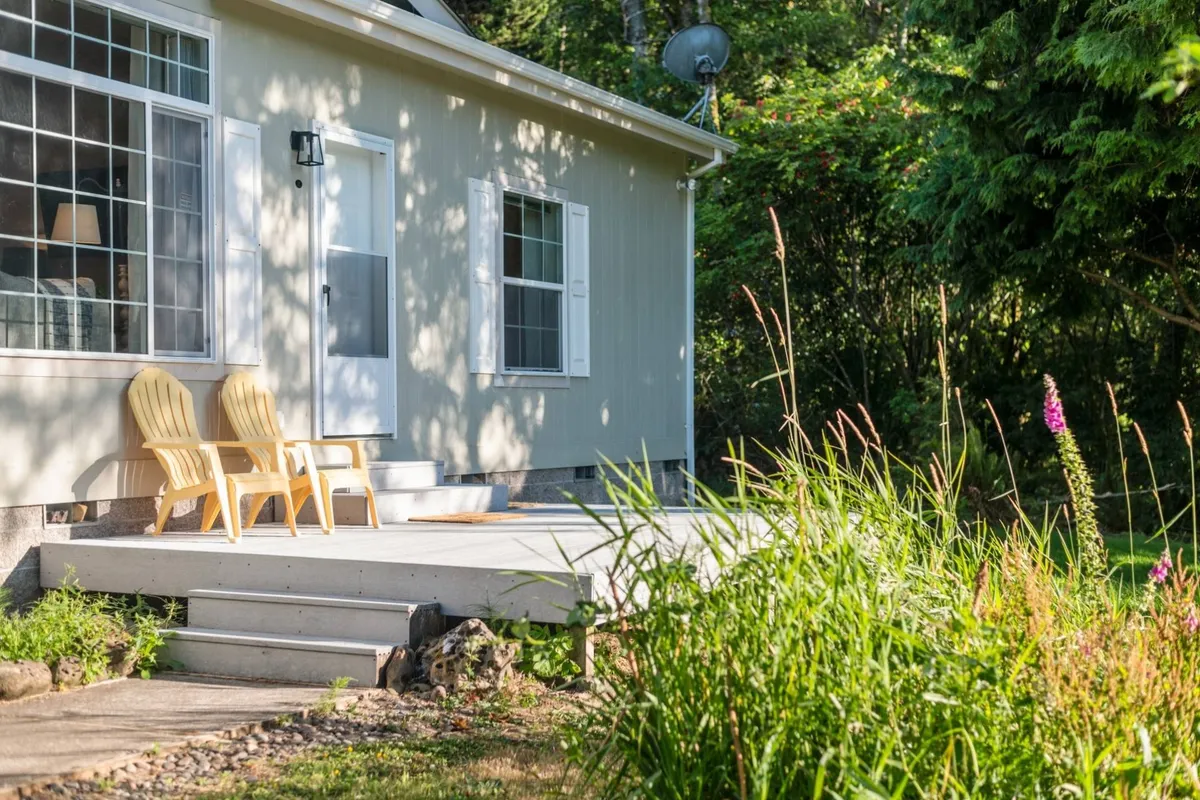 The image shows two inviting yellow chairs on the front porch, positioned to overlook the surrounding landscape through a large window near the front door. The scene feels welcoming, peaceful, and ideal for morning coffee or unwinding while soaking in nature.