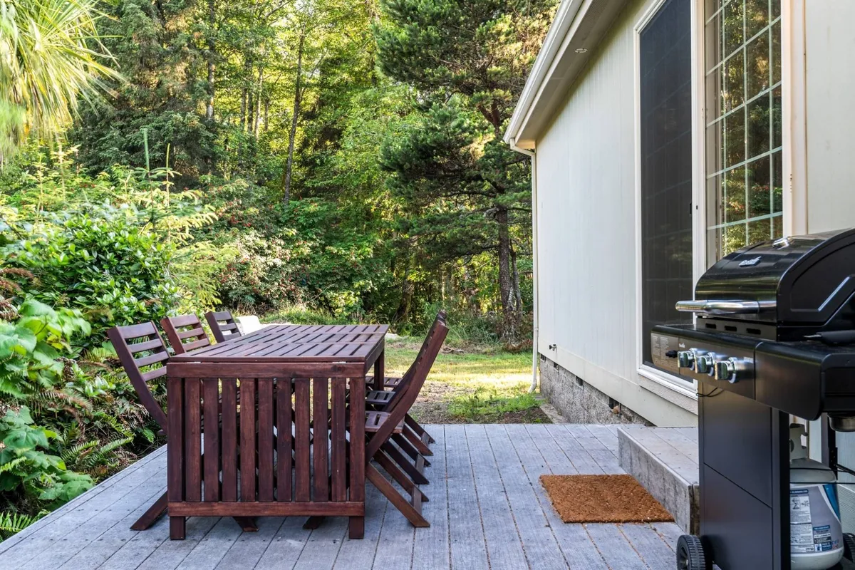 This exterior scene features a wooden dining table and grill surrounded by lush greenery, ideal for outdoor dining and social gatherings under the stars. The setting invites guests to imagine memorable summer nights and special occasions shared with loved ones.